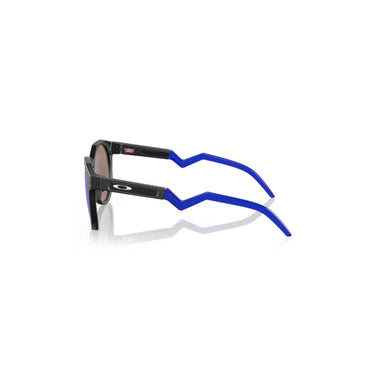 "gafas de sol con lentes redondas de color azul reflectante. El marco es negro y las patillas tienen un diseño distintivo con una curva y detalles en azul. En una de las patillas se encuentra el logotipo de la marca Oakley."