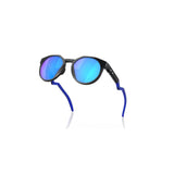 "gafas de sol con lentes redondeadas y reflectantes en tonos azules. El marco es negro y las patillas tienen un diseño curvado con detalles en azul. En una de las patillas se puede observar el logotipo de la marca Oakley."