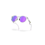 "Unas gafas de sol con montura transparente y lentes redondas de color morado. La patilla derecha muestra el logotipo de "Oakley"."